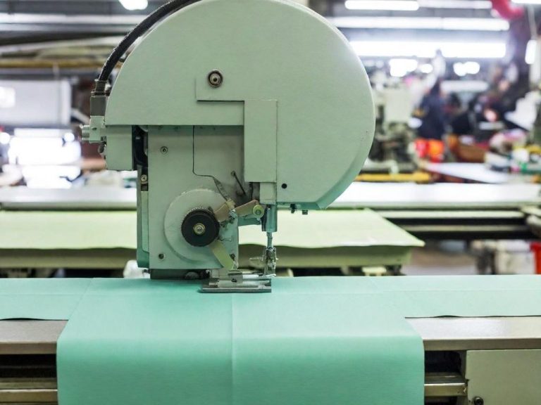 Máquina de corte industrial sobre tela verde en un taller de confección.