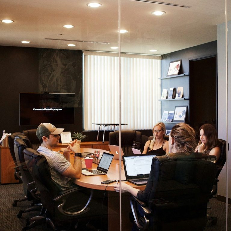 Grupo de personas en una sala de reuniones, trabajando en laptops y documentos.
