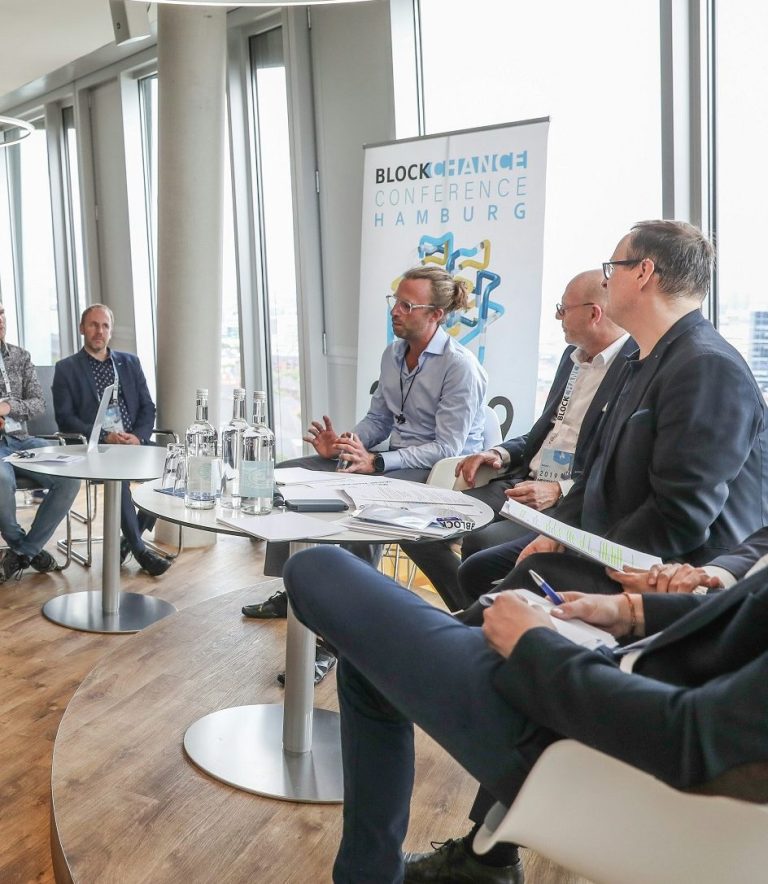 Panel de discusión con varios ponentes en un entorno moderno y luminoso.