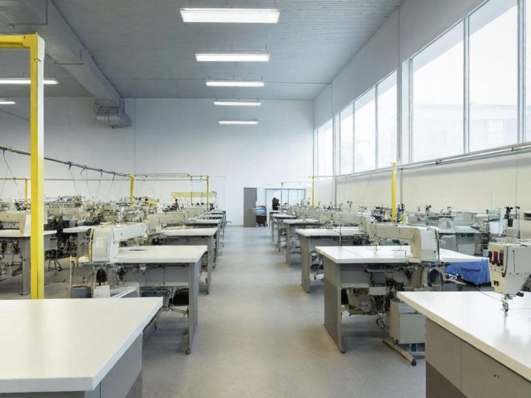 Taller de costura con máquinas, mesas y gran iluminación natural.